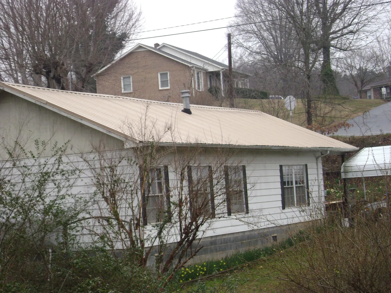 Tan metal roof on a white sided house set into a hillside — Commercial Roofing by Roofing Brothers in Aberdeen
